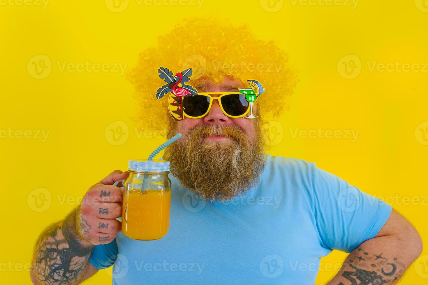 Fat happy man with wig in head and sunglasses drinks a fruit juice photo