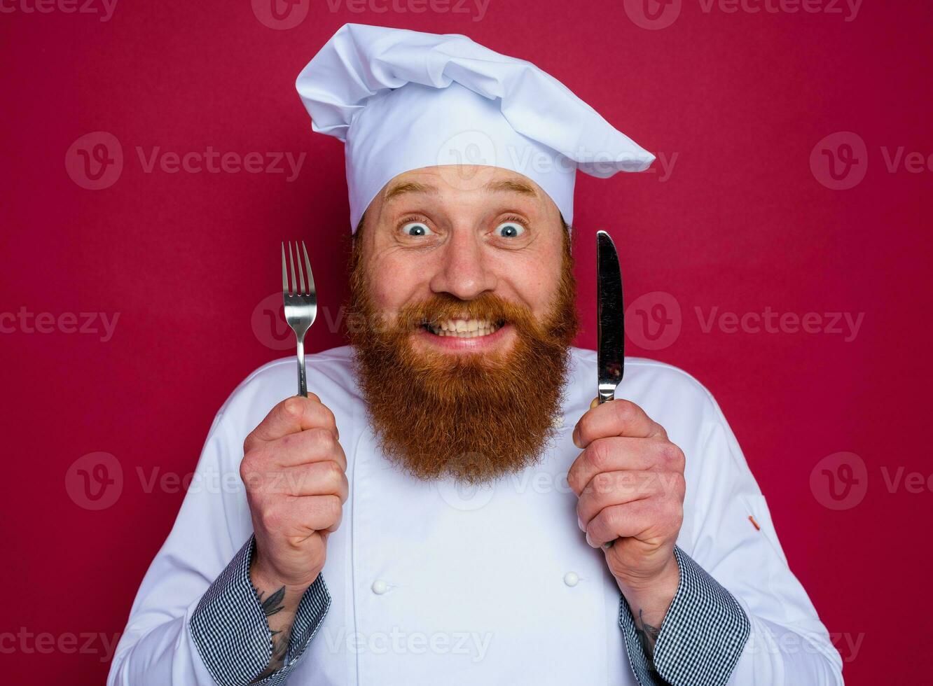 happy chef with beard and red apron holds cutlery in hand photo