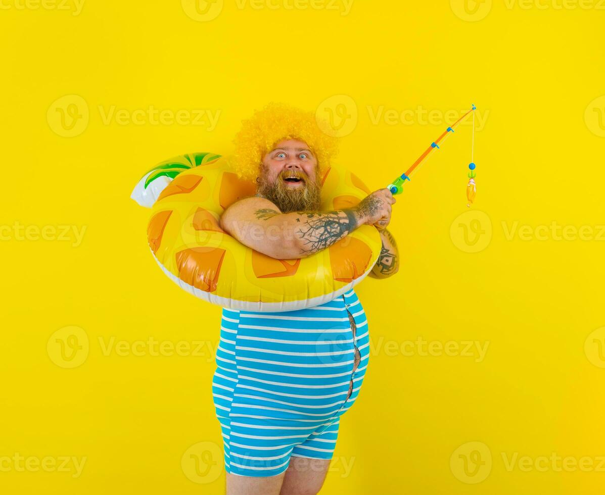Fat happy man with wig in head plays with the fishing rod photo