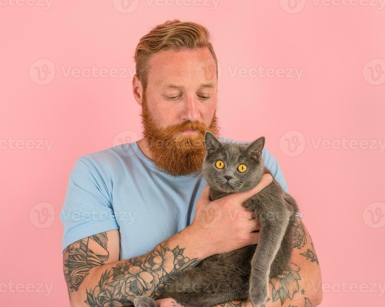 Man with beard and tattoos caresses a grey cat photo