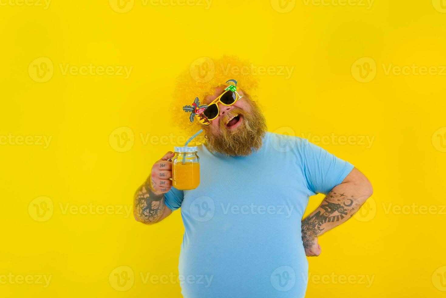 Fat happy man with wig in head and sunglasses drinks a fruit juice photo