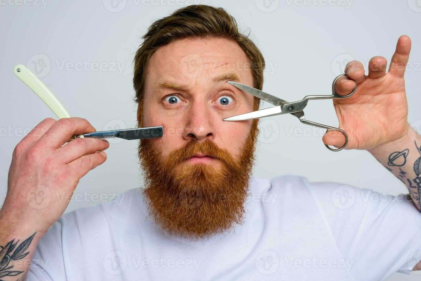 Worried man with scissors and blade is ready to cut the beard photo