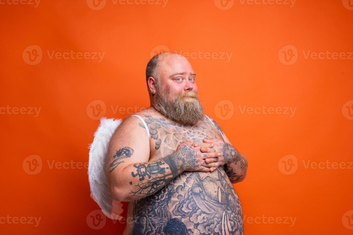 Fat man with beard ,tattoos and wings acts like an angel photo