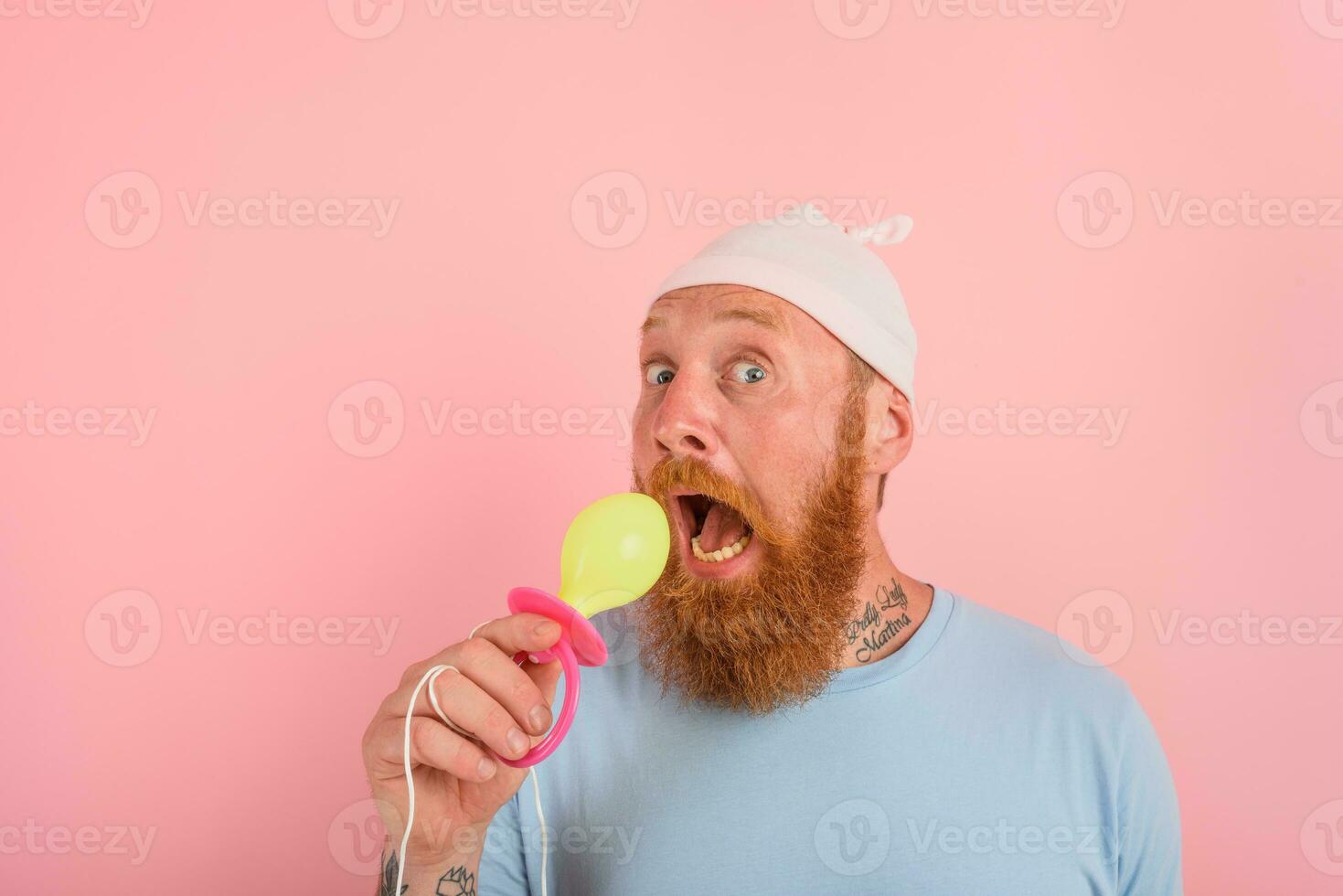 Man with beard and tattoos acts like a little newborn baby with pacifier in hand photo