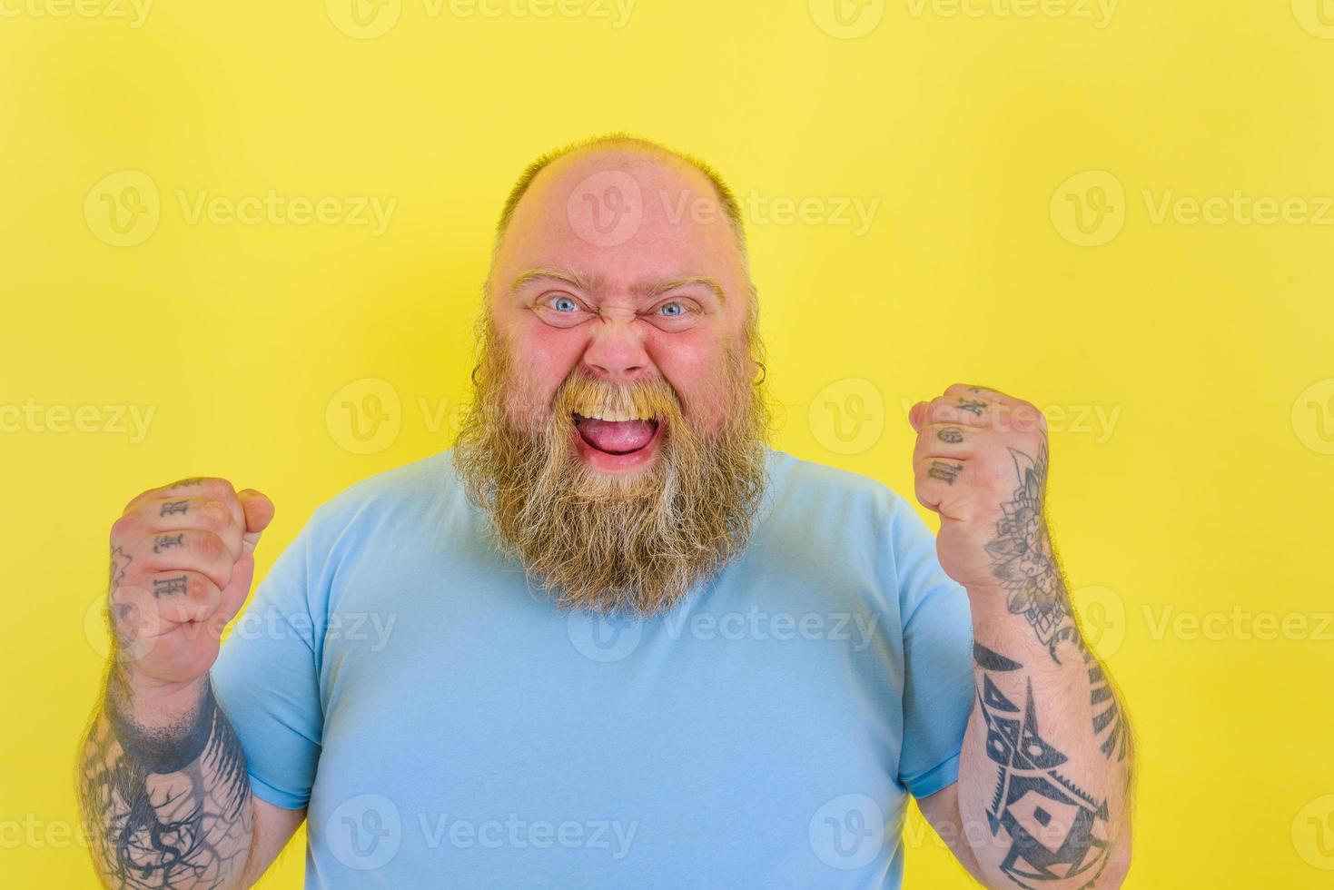 contento hombre con barba y tatuajes lo hace un victorioso gesto con manos foto