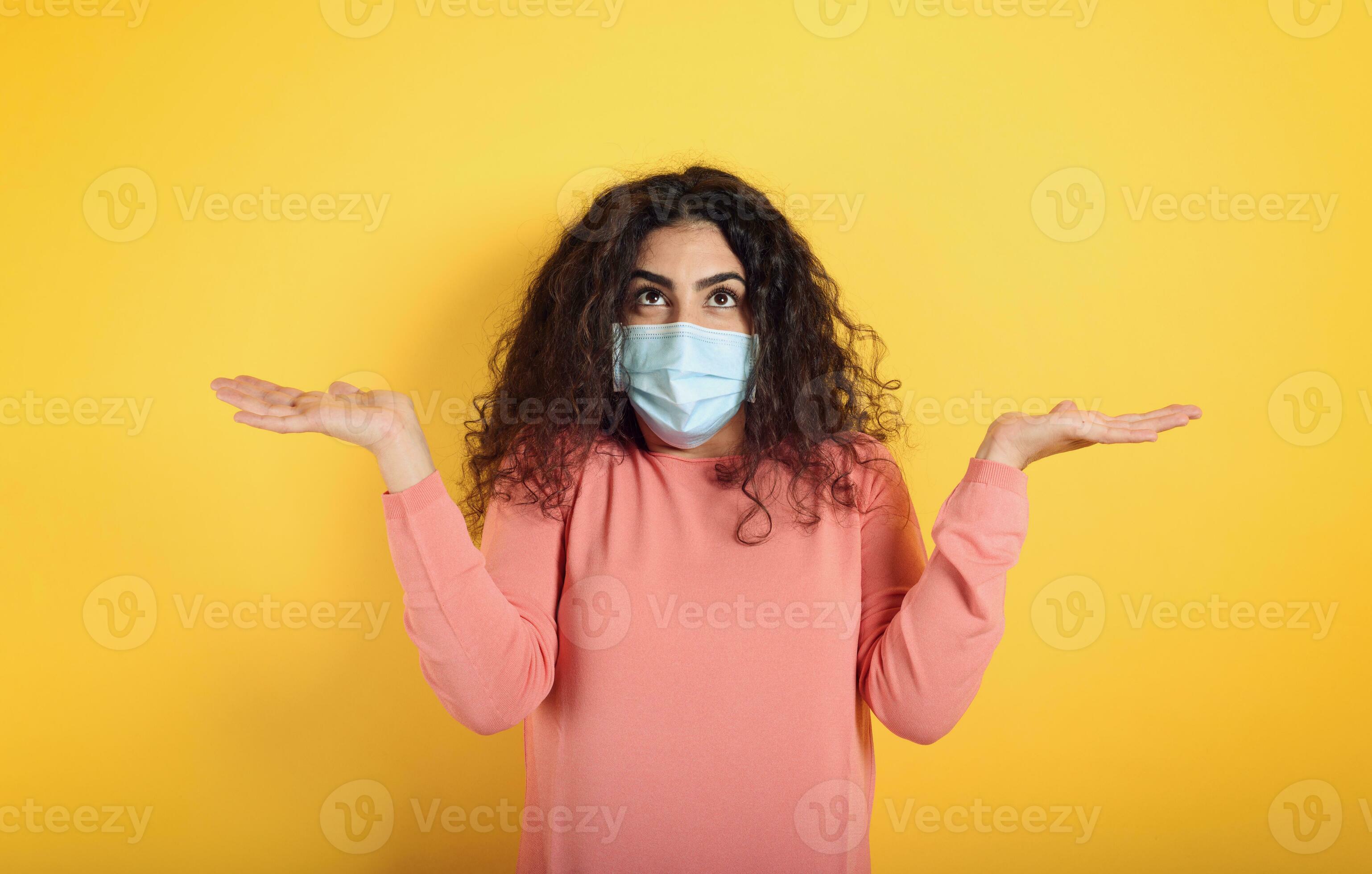 Girl with face mask is confused about covid 19. Yellow background