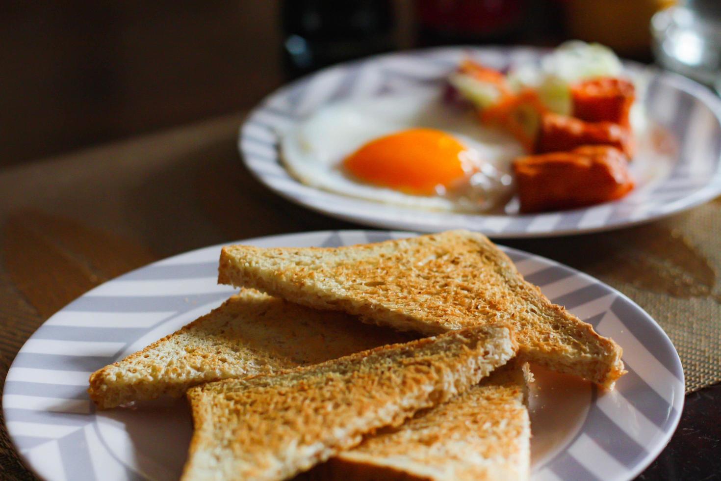 Breakfast, fried eggs, fried sausage, vegetable salad and toast on a brown wooden table with coffee. photo