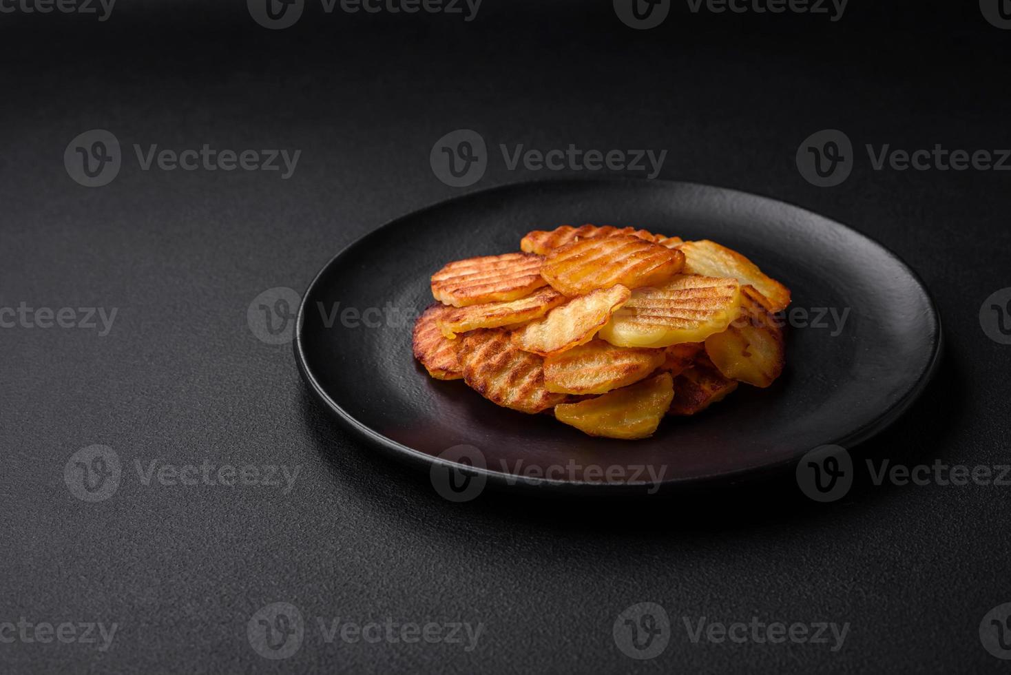 Delicious crispy fried potatoes in slices on a black ceramic plate photo