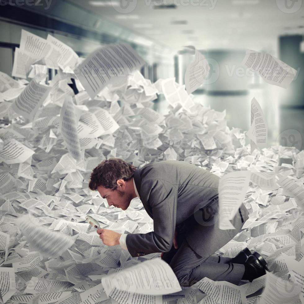 Businessman looking with magnifying glass in the middle of a flood of sheets photo