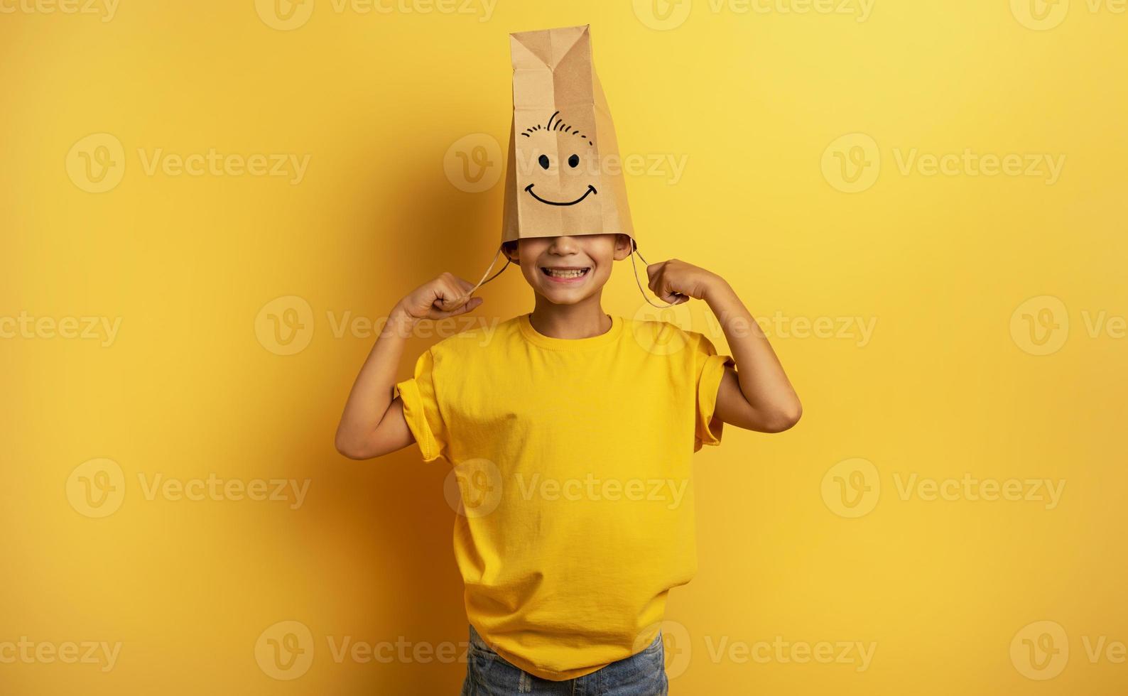 Child hides his head inside a shopping bag. yellow background photo