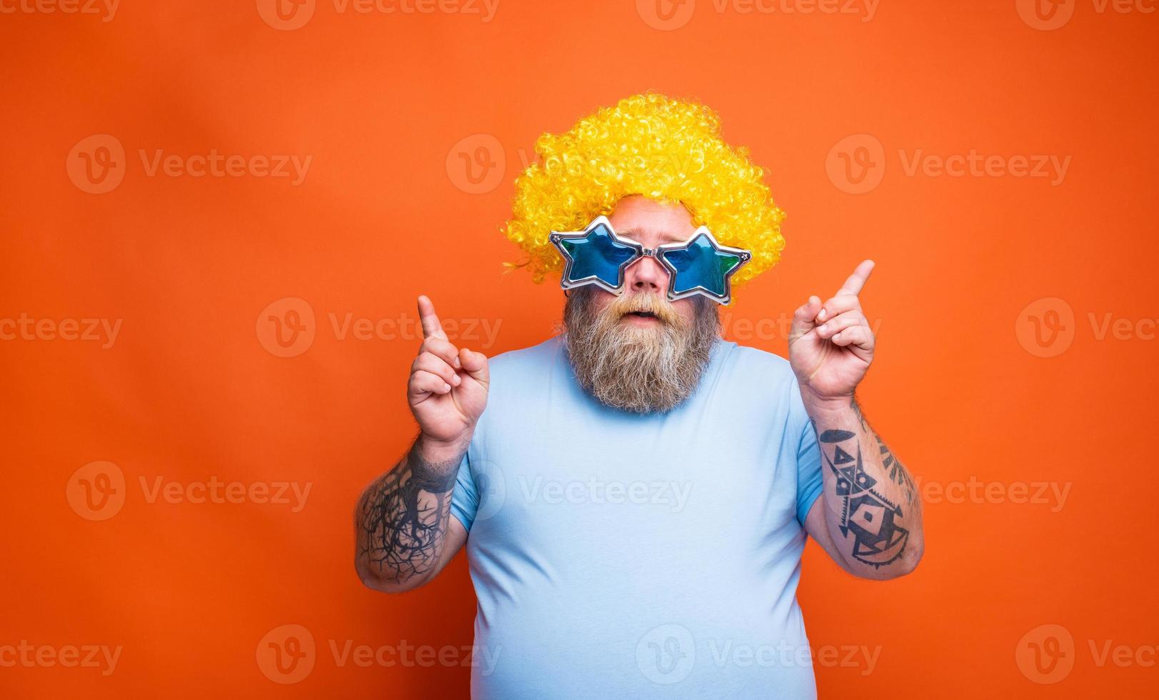 Fat thoughtful man with beard, tattoos and sunglasses dances music on a disco photo