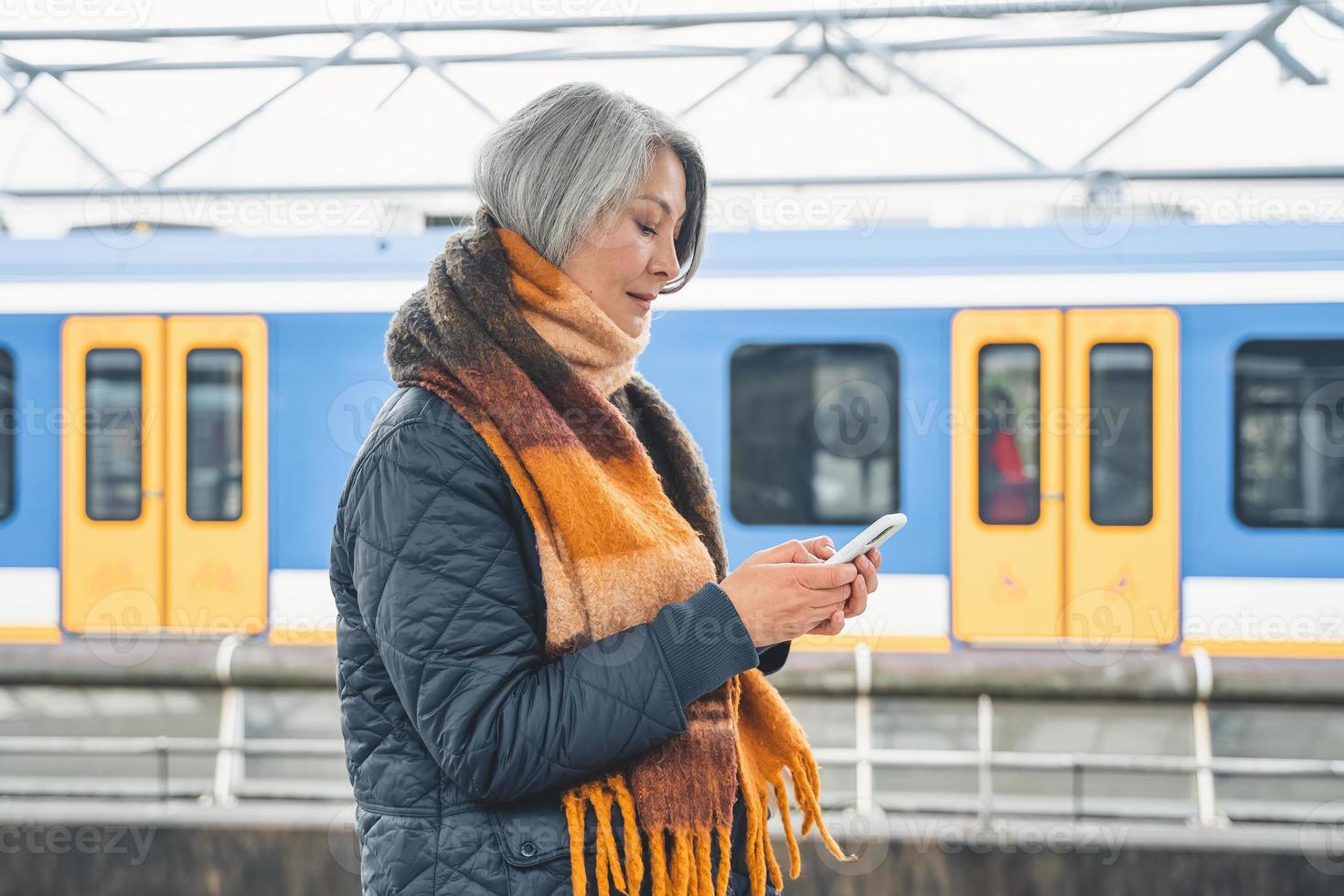 Senior woman send message with a mobile phone and waits for a train photo