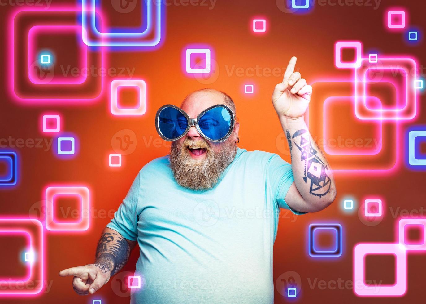 Fat happy man with beard, tattoos and sunglasses dances music photo