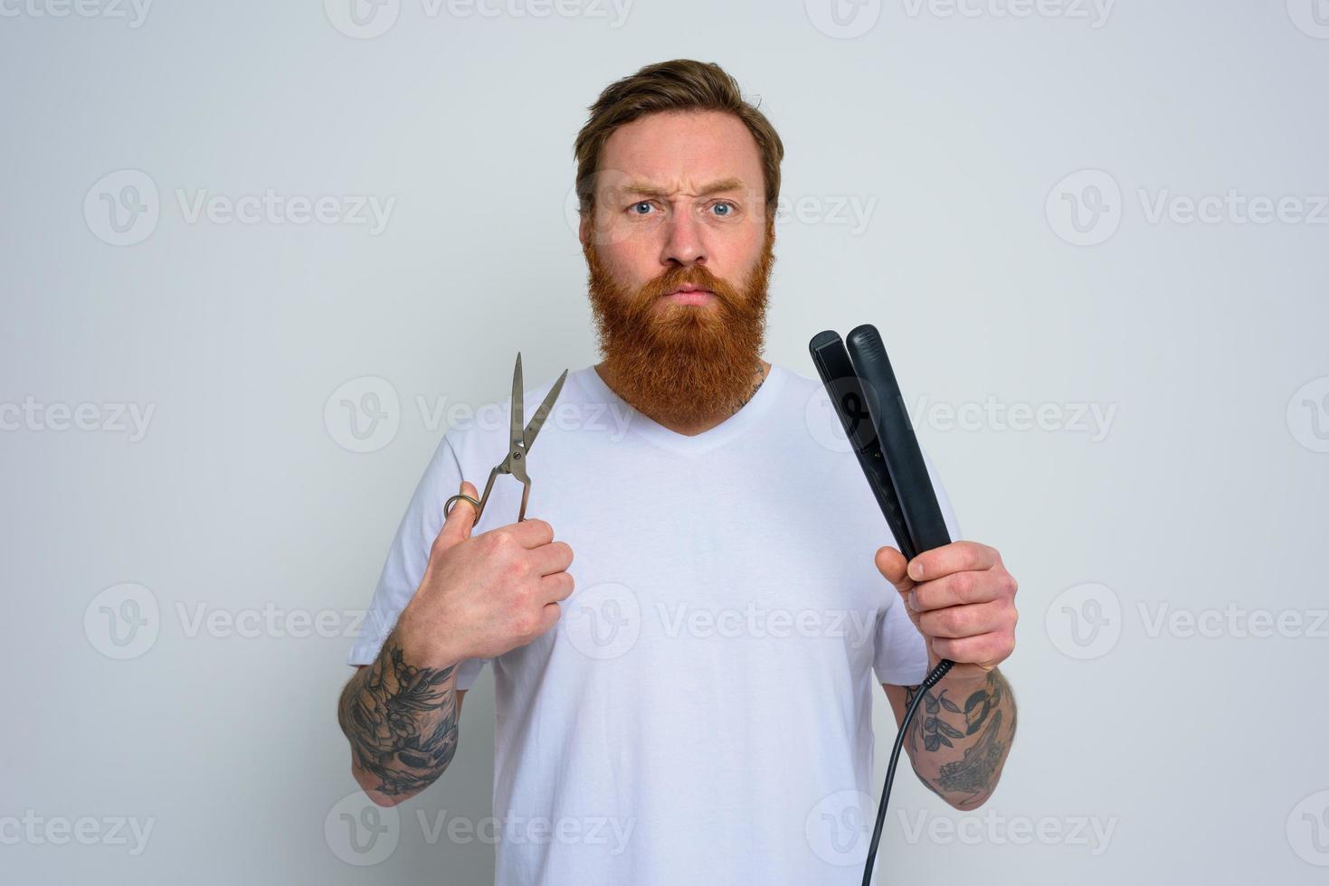 Undecided man with scissors and straightener is ready to work with hair photo