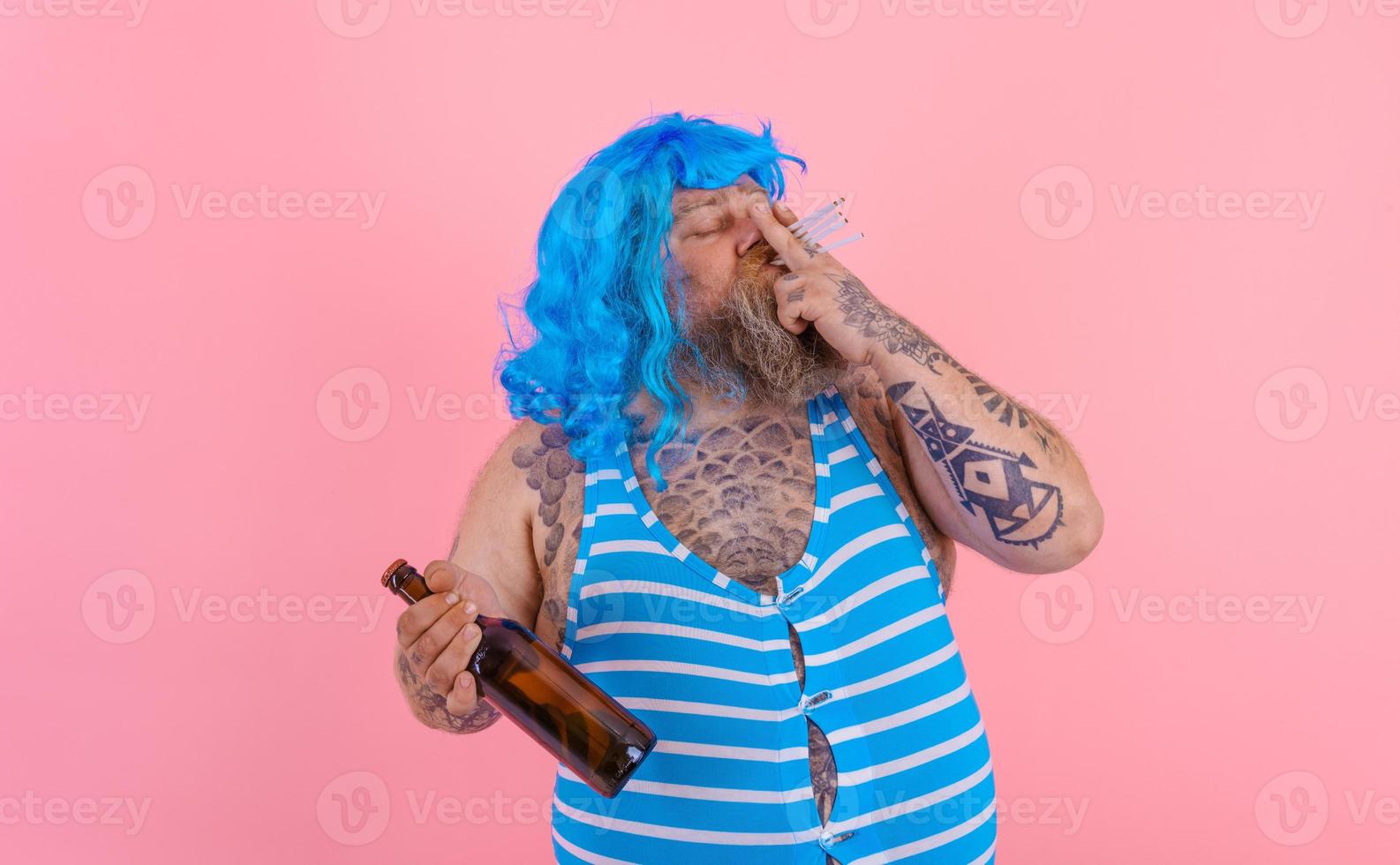 Fat man with beard and wig smokes cigarettes and drinks beer photo