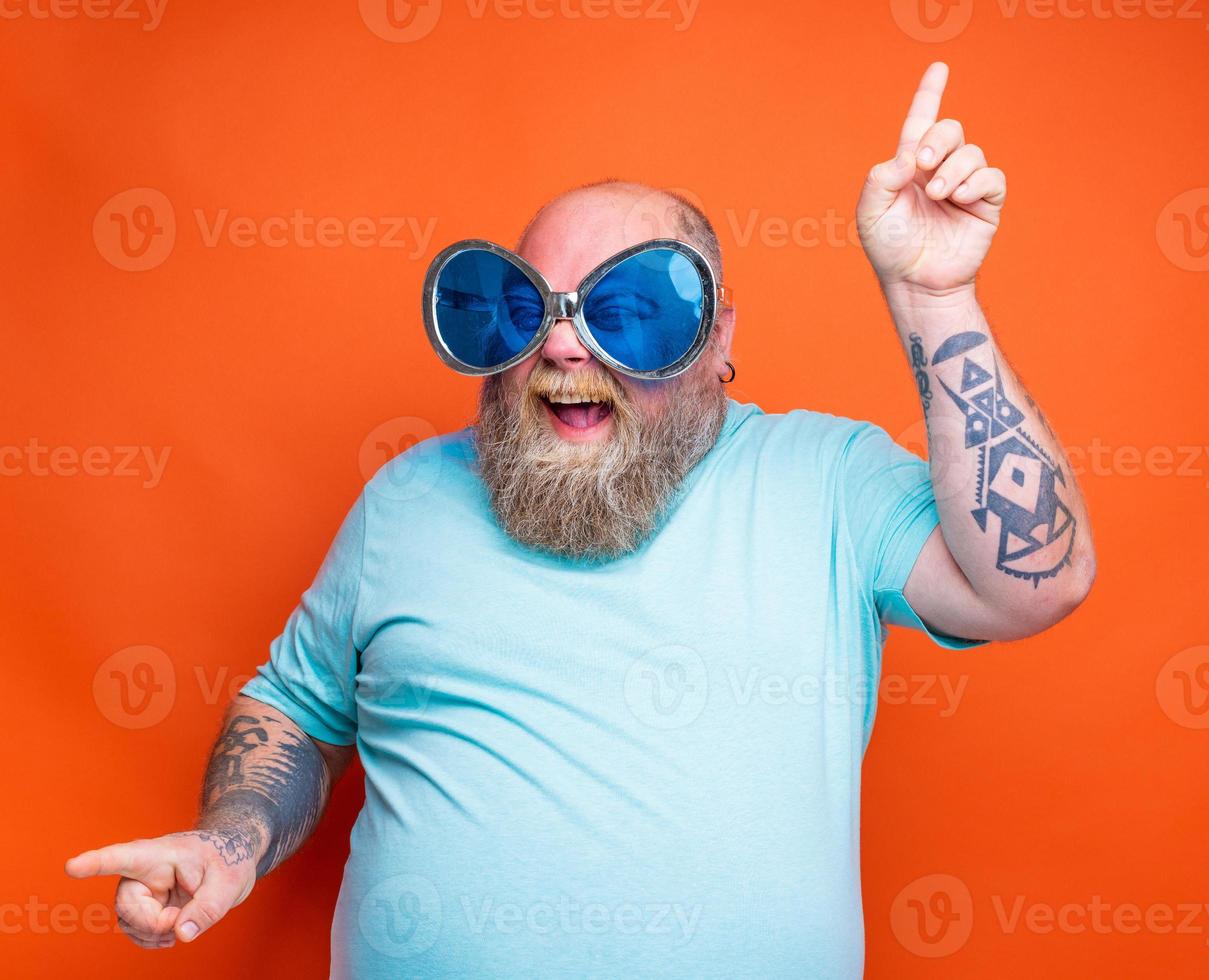 Fat happy man with beard, tattoos and sunglasses dances music photo
