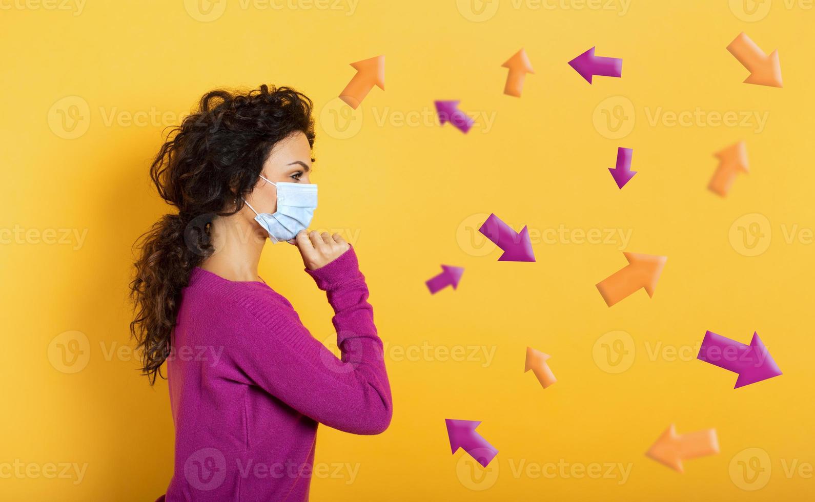 Girl with face mask is undecided about the arrow to follow. Concept of covid-19 confusion. Yellow background photo