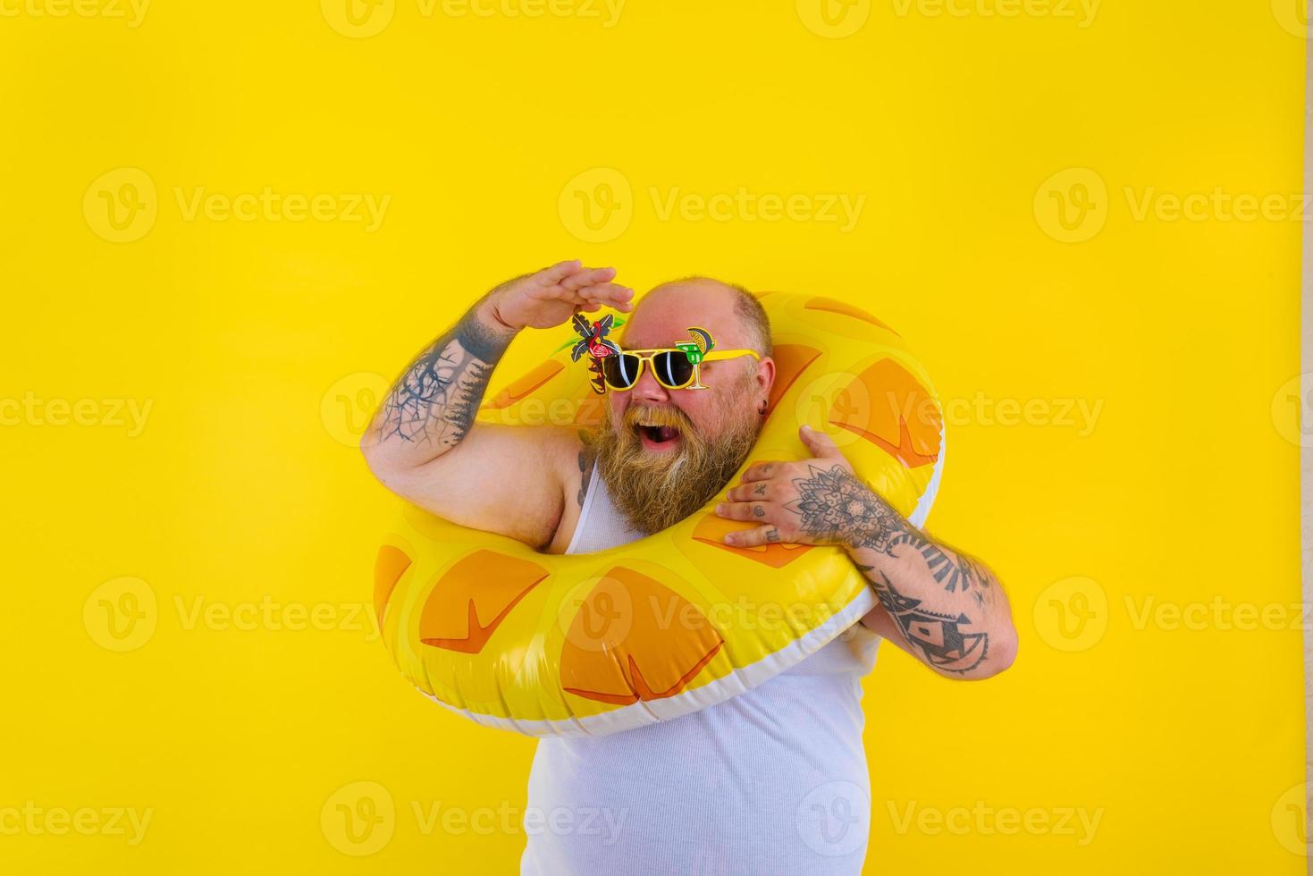 Fat happy man with wig in head is ready to swim with a donut lifesaver photo