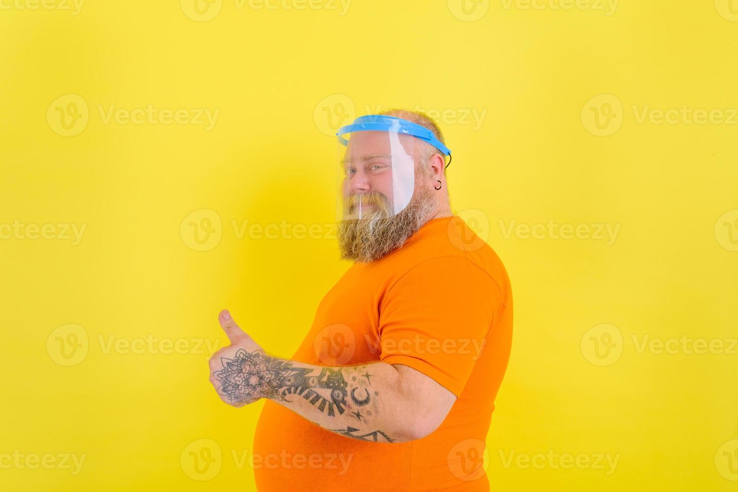 Happy man with beard and tattoos wears a protective face shield against covid-19 photo