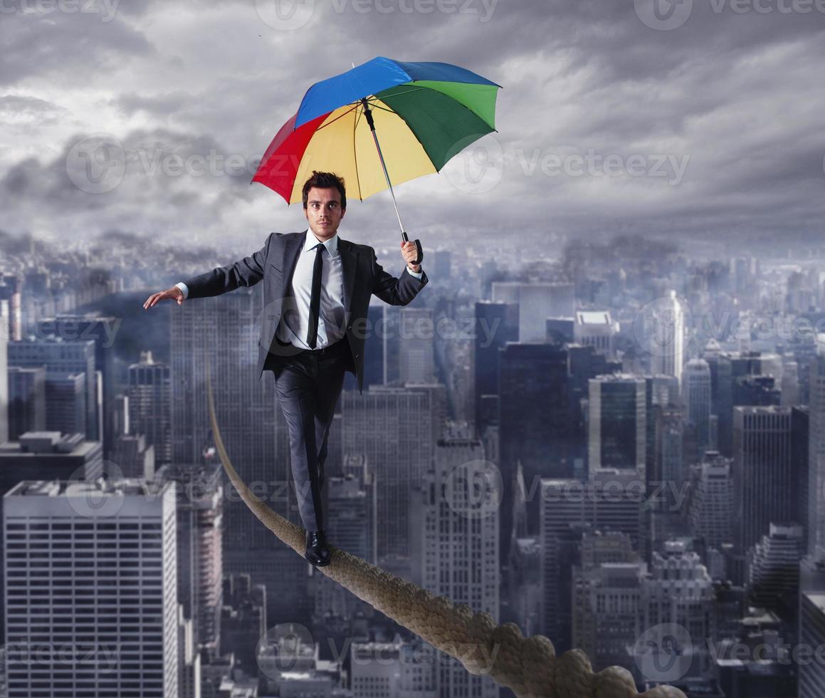 Equilibrist businessman walk on a rope with umbrella over the city. Concept of overcome the problems and positivity photo