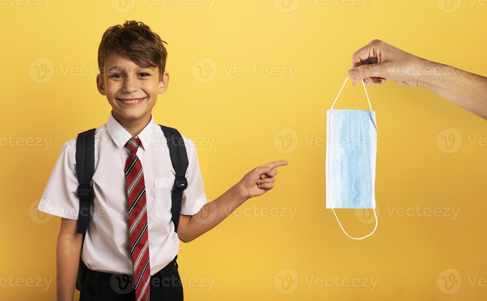Young smiling student indicates a face mask for covid19. yellow background photo