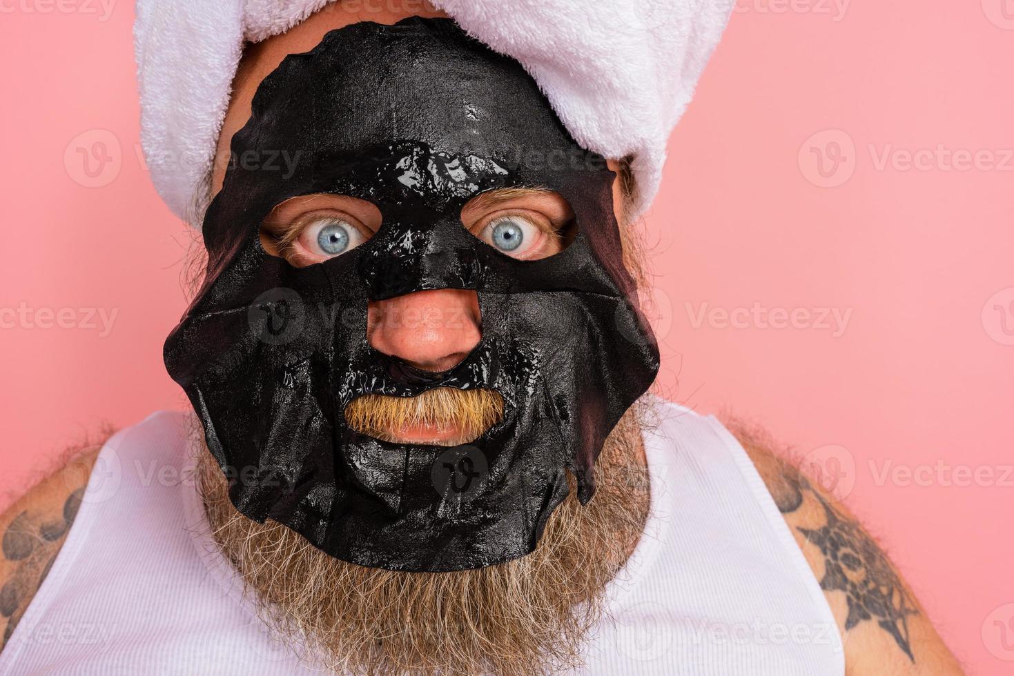 Doubter man with beard acts like a woman and has fun with a facial mask photo