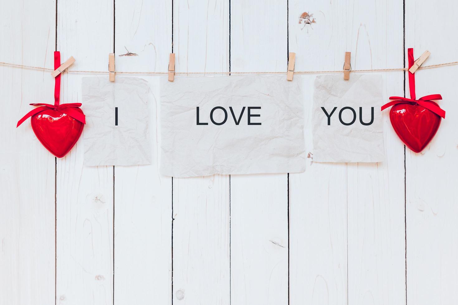 Red heart and old paper with text I LOVE YOU hanging at clothesline on wood white background. photo