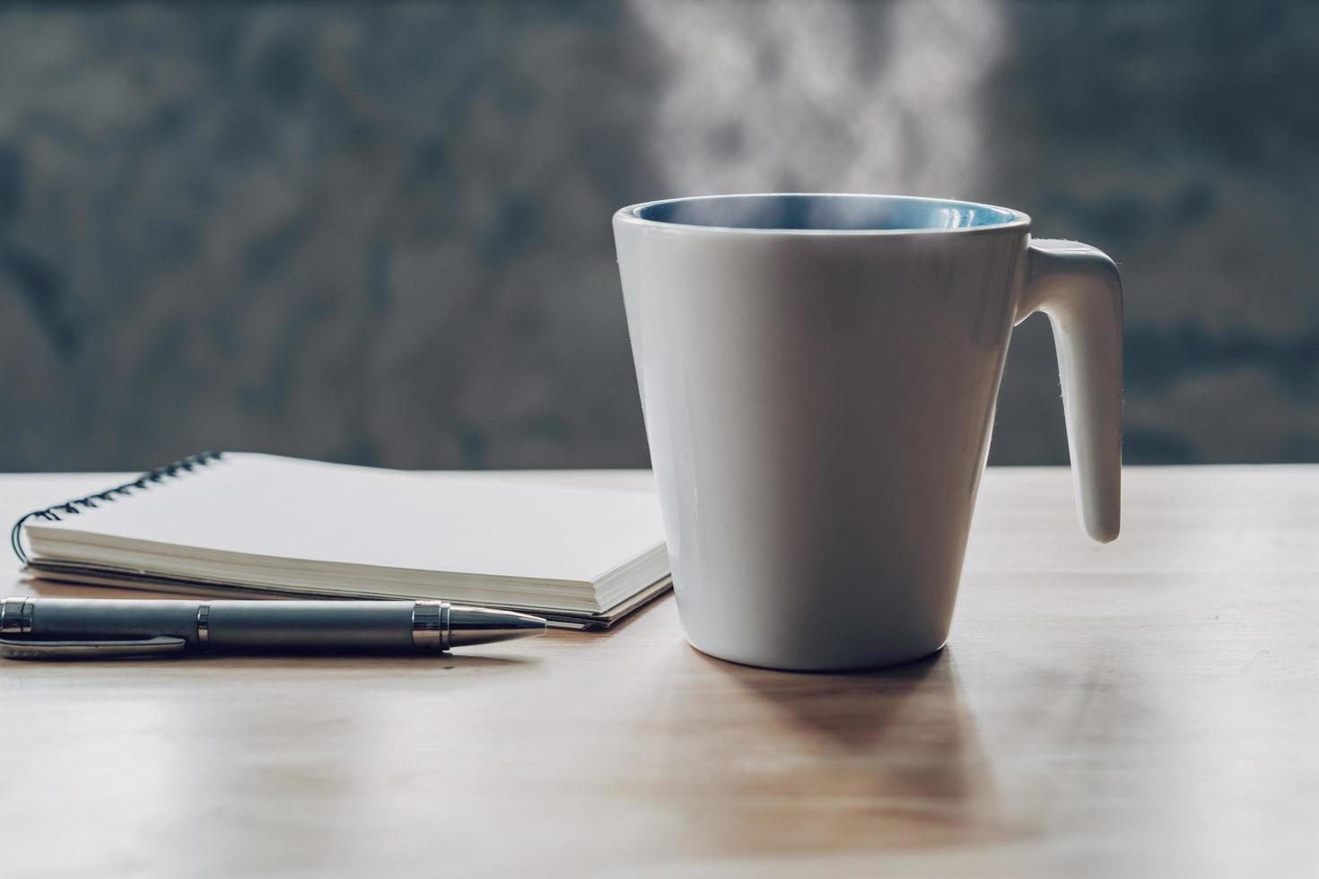 cup of coffee and notepad with pen on wood table photo