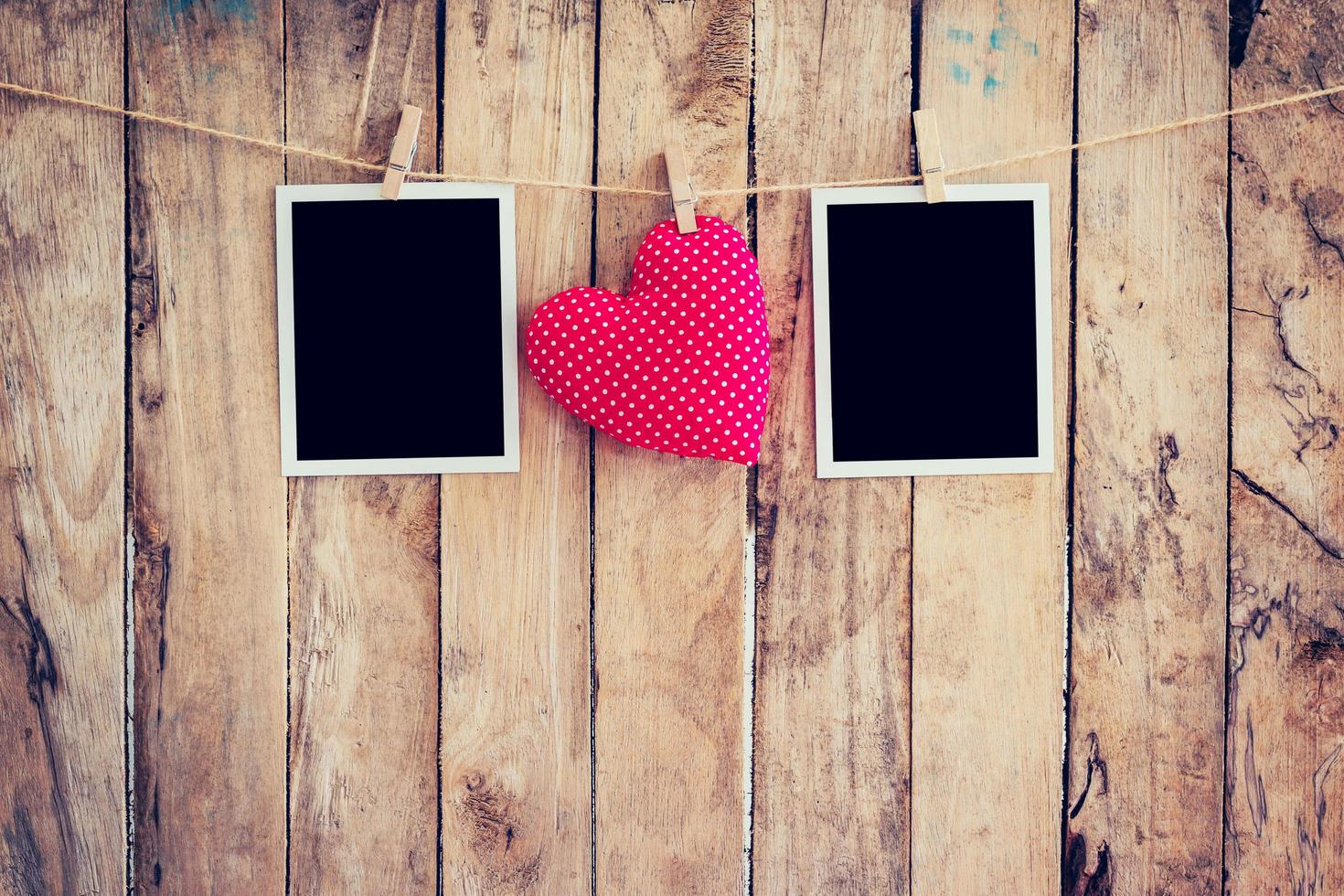 Red heart and two photo frame hanging on clothesline rope with wooden background.