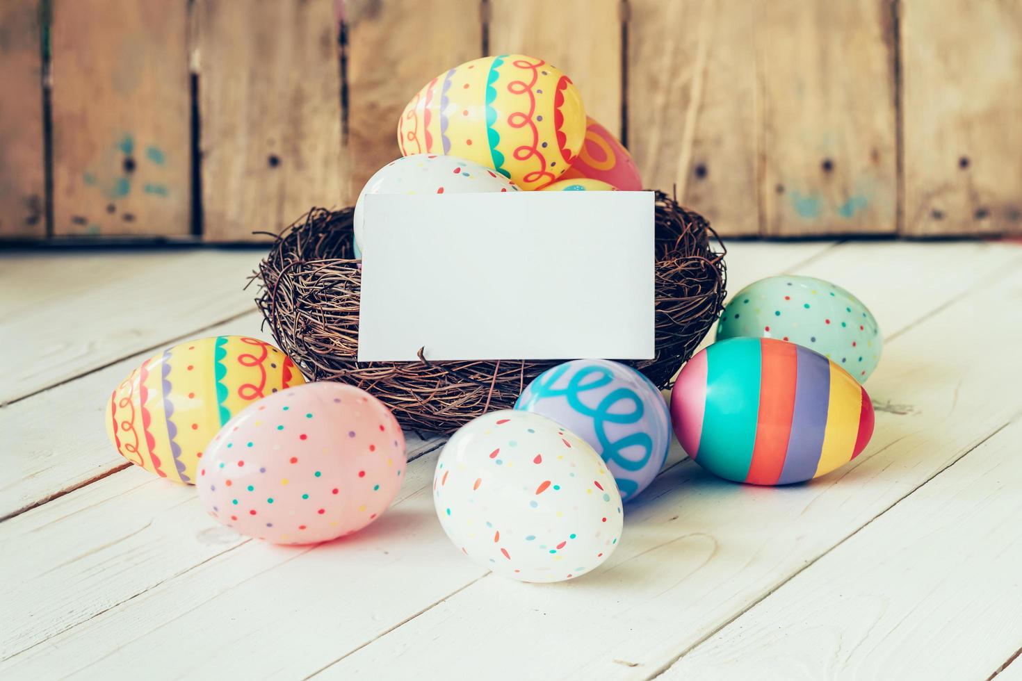 Colorful easter eggs in the nest and paper card on wood table background. photo