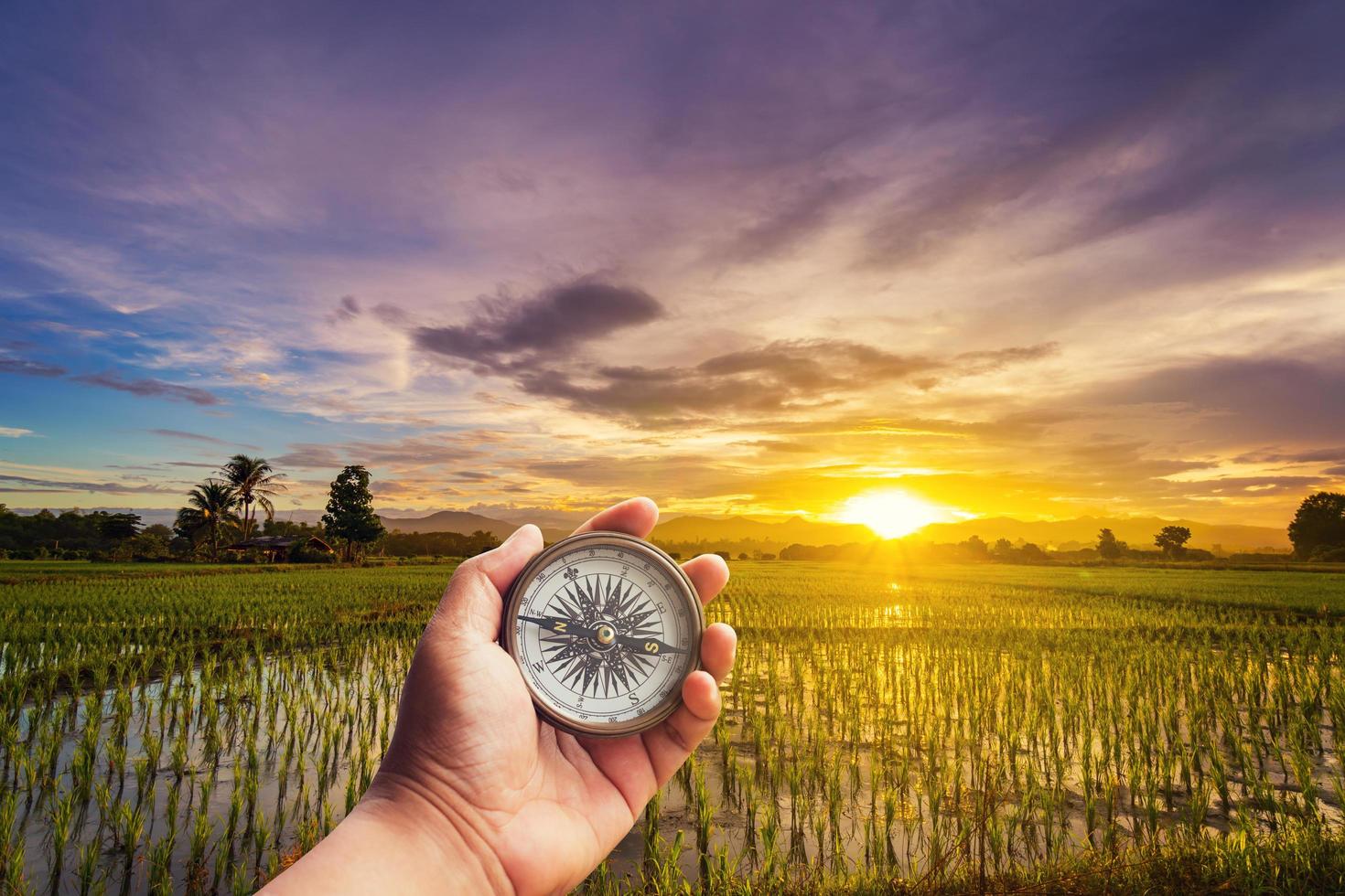 un hombre participación Brújula en mano a campo y puesta de sol para navegación guía. foto