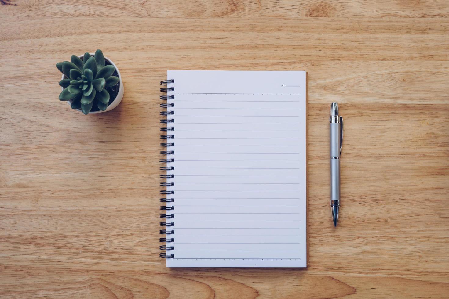 Blank notebook and pencil on wood table with pot plant. photo