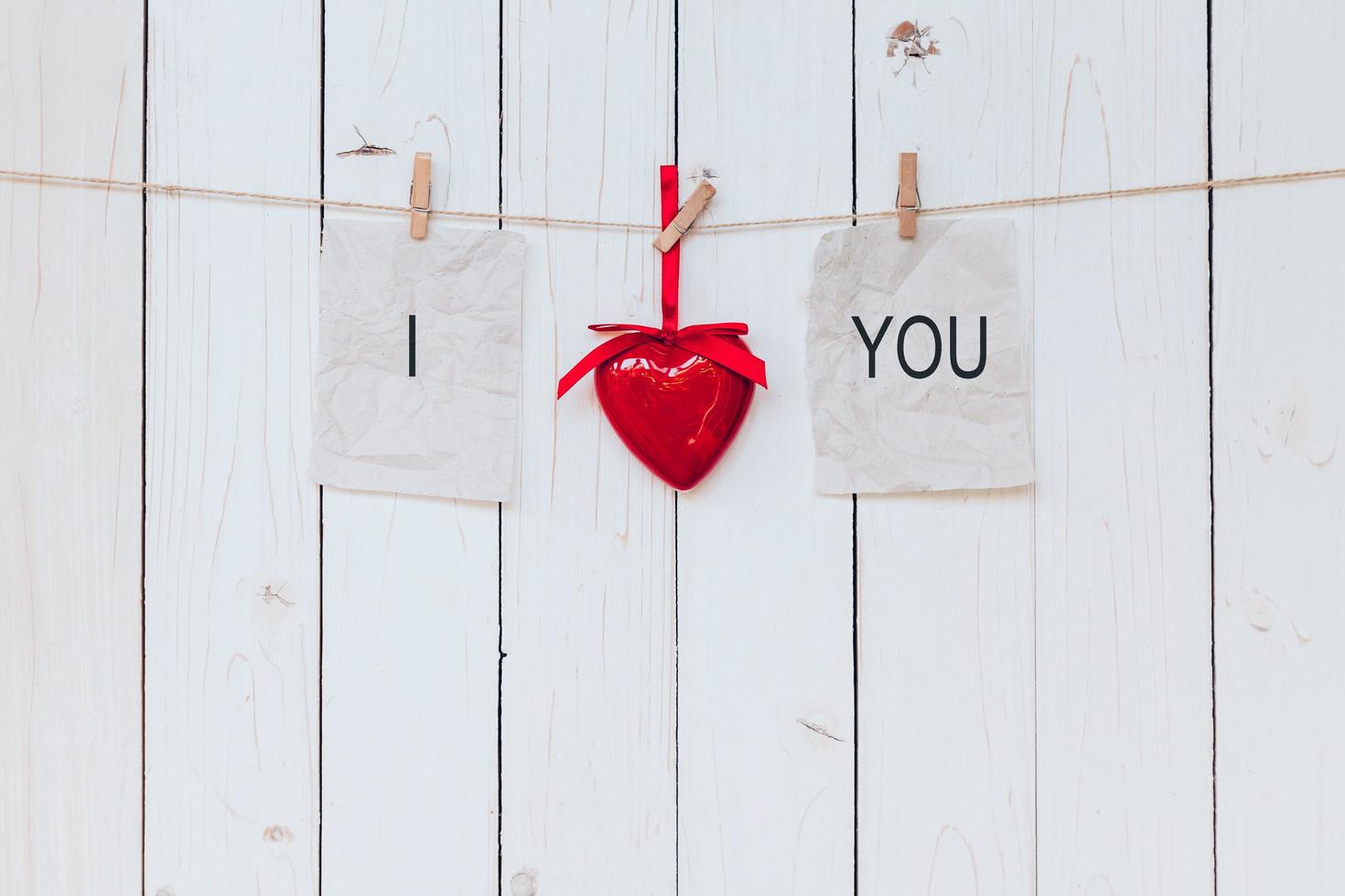 rojo corazón y antiguo papel con texto yo amor usted colgando a tendedero en madera blanco antecedentes. foto