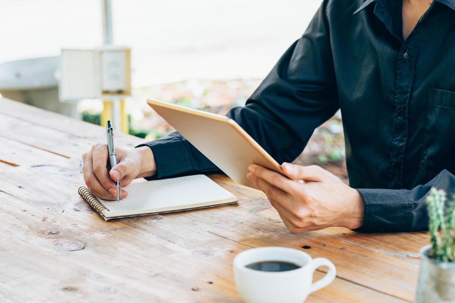 Business man hand holding tablet and writing notebook in coffee shop. photo