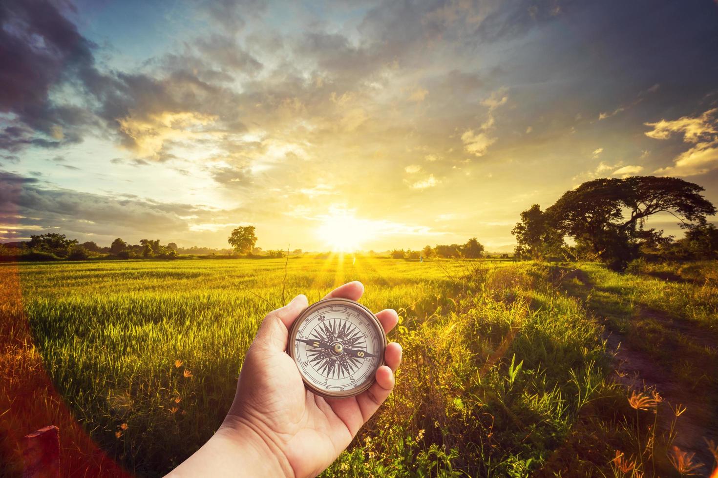 un hombre participación Brújula en mano a campo y puesta de sol para navegación guía. foto