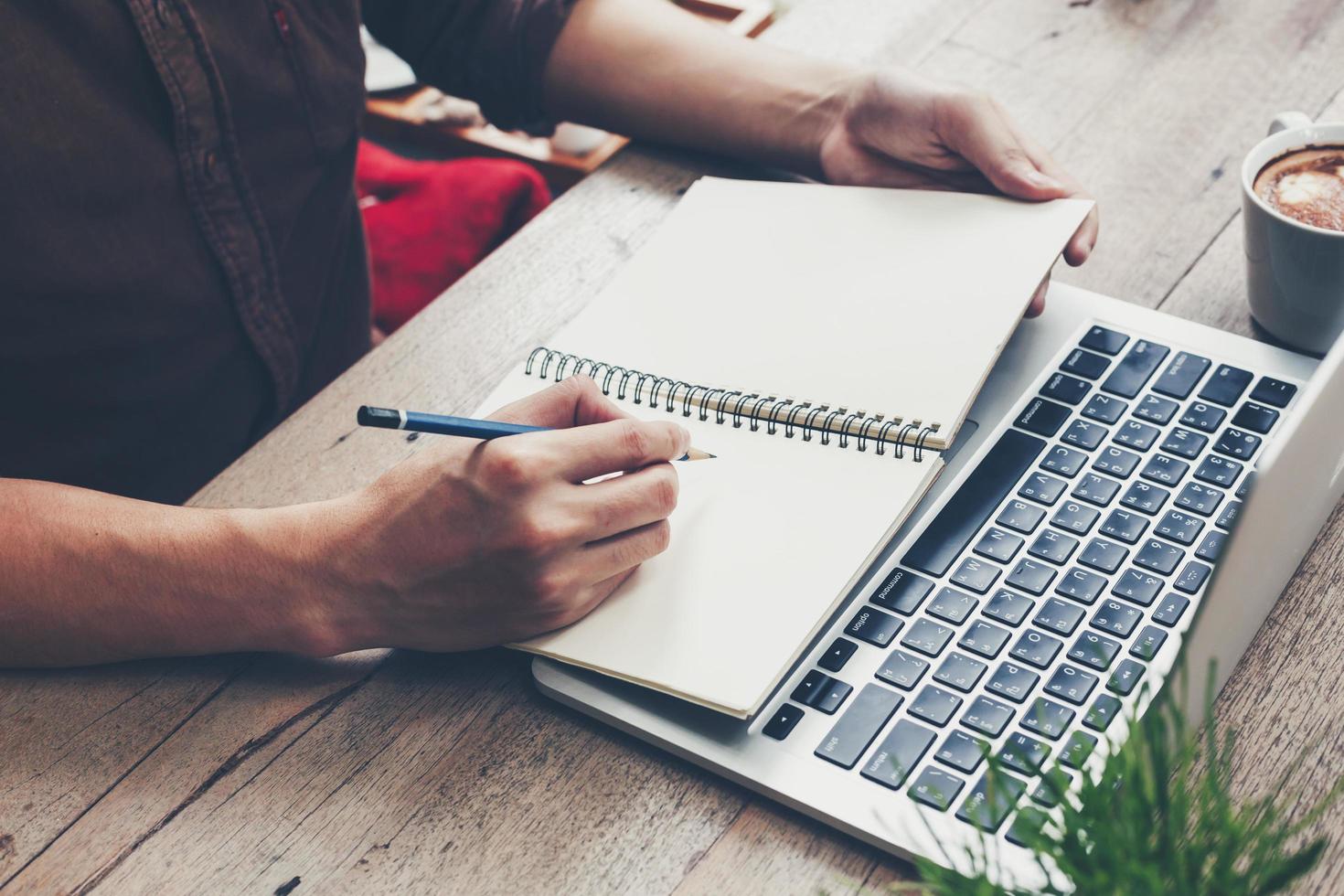 Young business man hand writing notebook and using laptop on wood table. photo