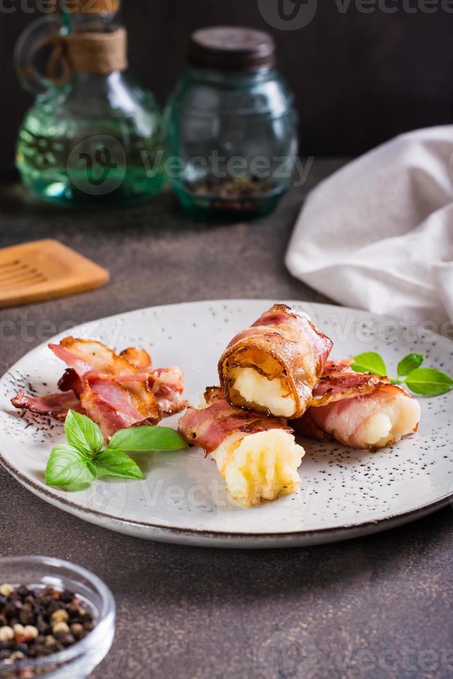 Mashed potatoes wrapped in fried bacon on a plate on the table. Vertical view photo