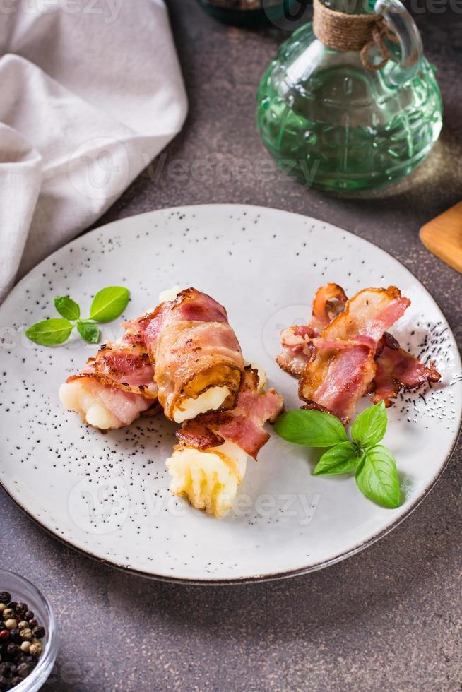 Rolls of fried bacon and mashed potatoes and basil on a plate on the table. Vertical view photo