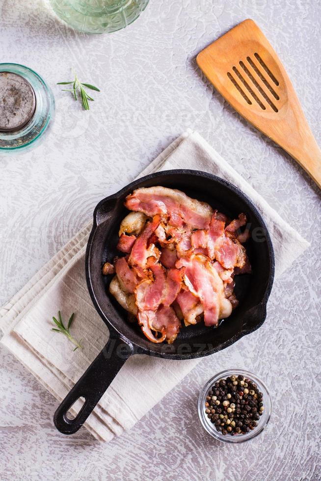 Crispy strips of bacon fried in a pan on the table. Top and vertical view photo