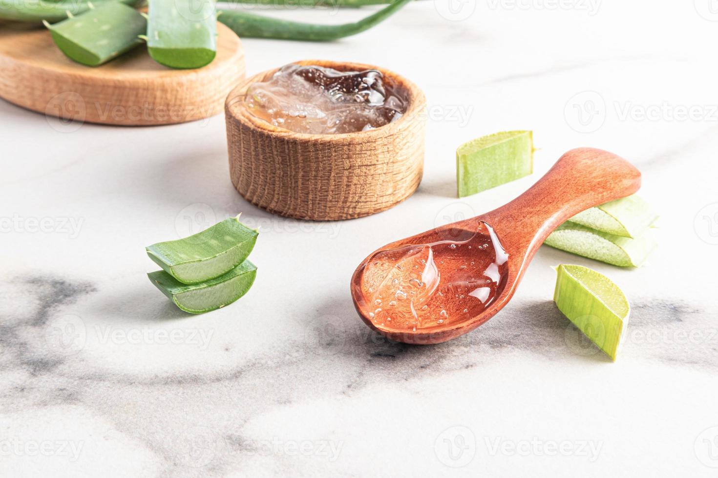 Aloe vera gel in a wooden spoon on a white marble table against a background of aloe leaves and a bowl of gel. a natural cosmetic for self-care. photo