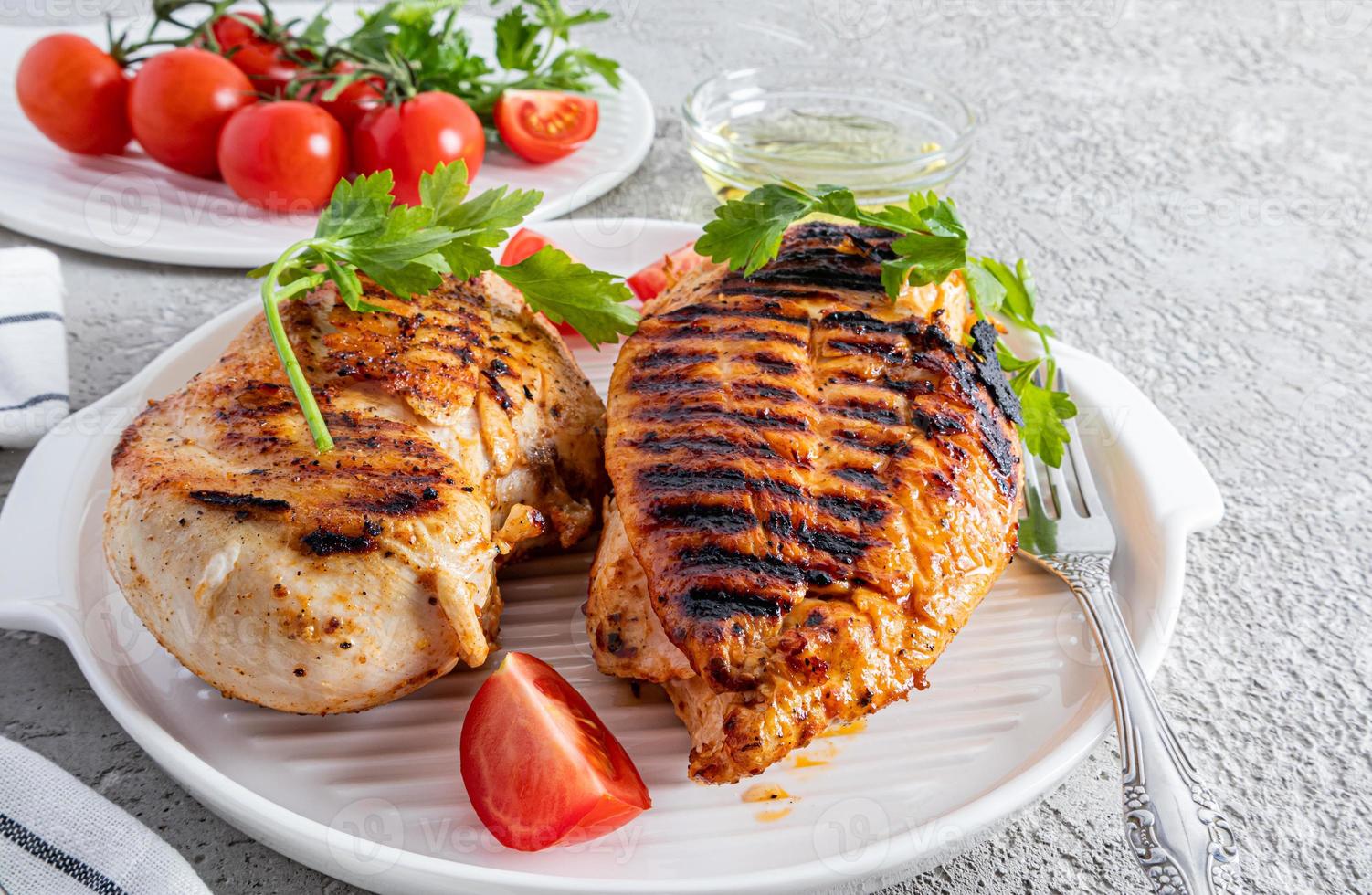 two juicy grilled chicken breasts on a white ceramic tray for serving with vegetables. front view. cement grey background. delicious food. photo