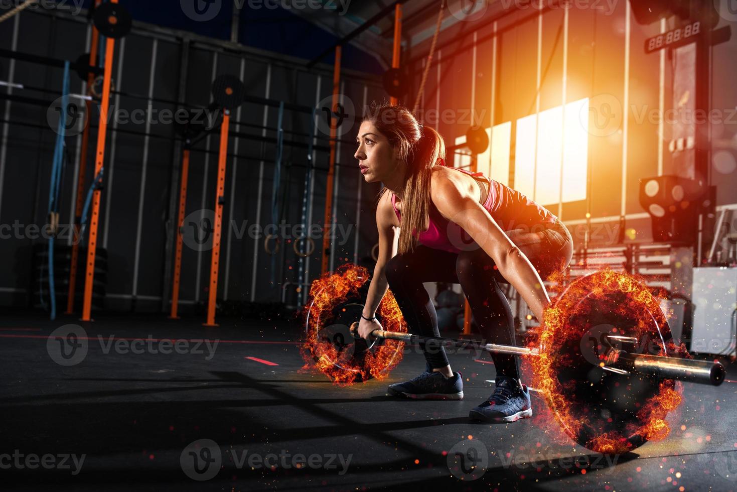 Athletic girl works out at the gym with a fiery barbell photo