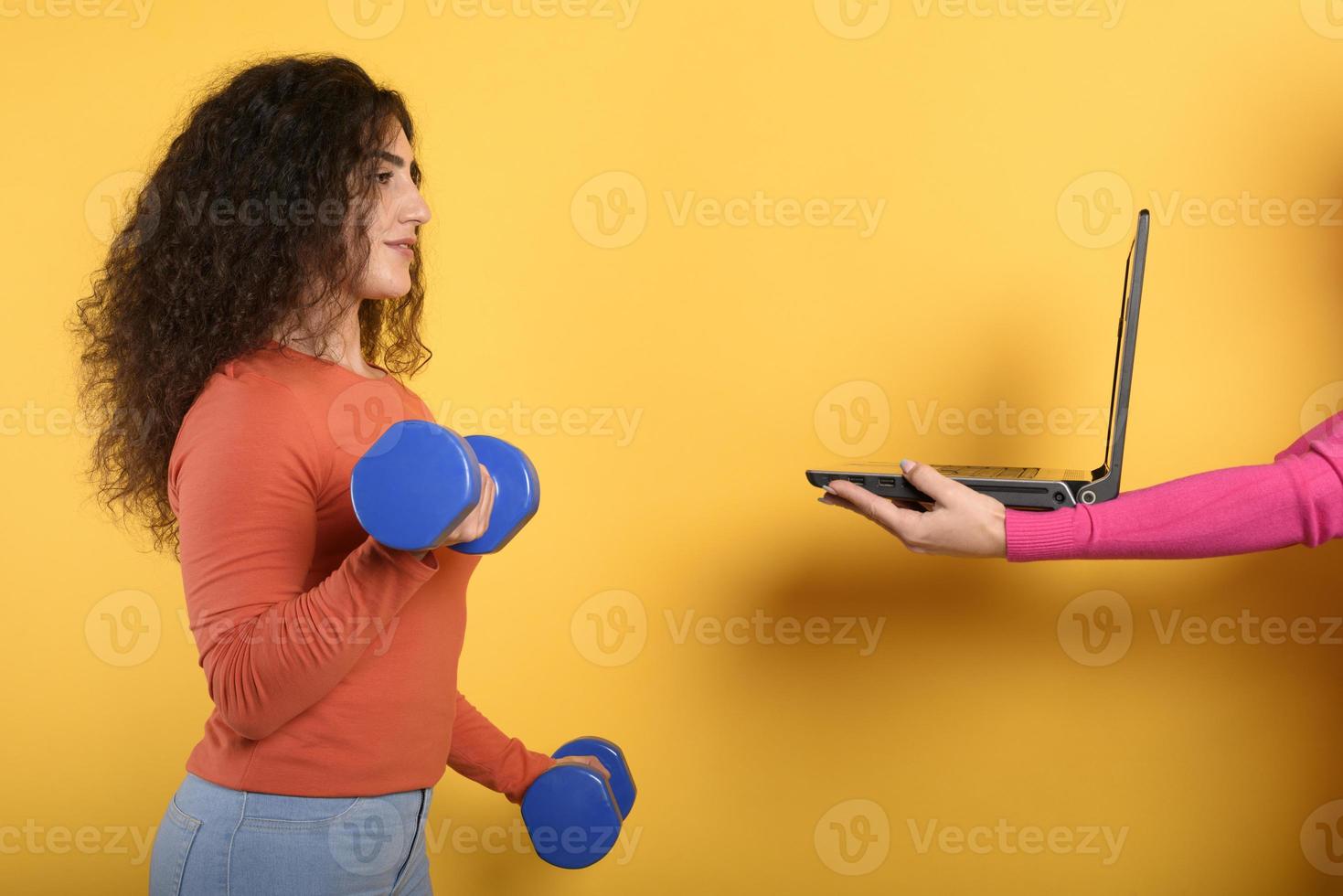 Girl with handlebars ready to start the gym online with a computer. yellow background photo