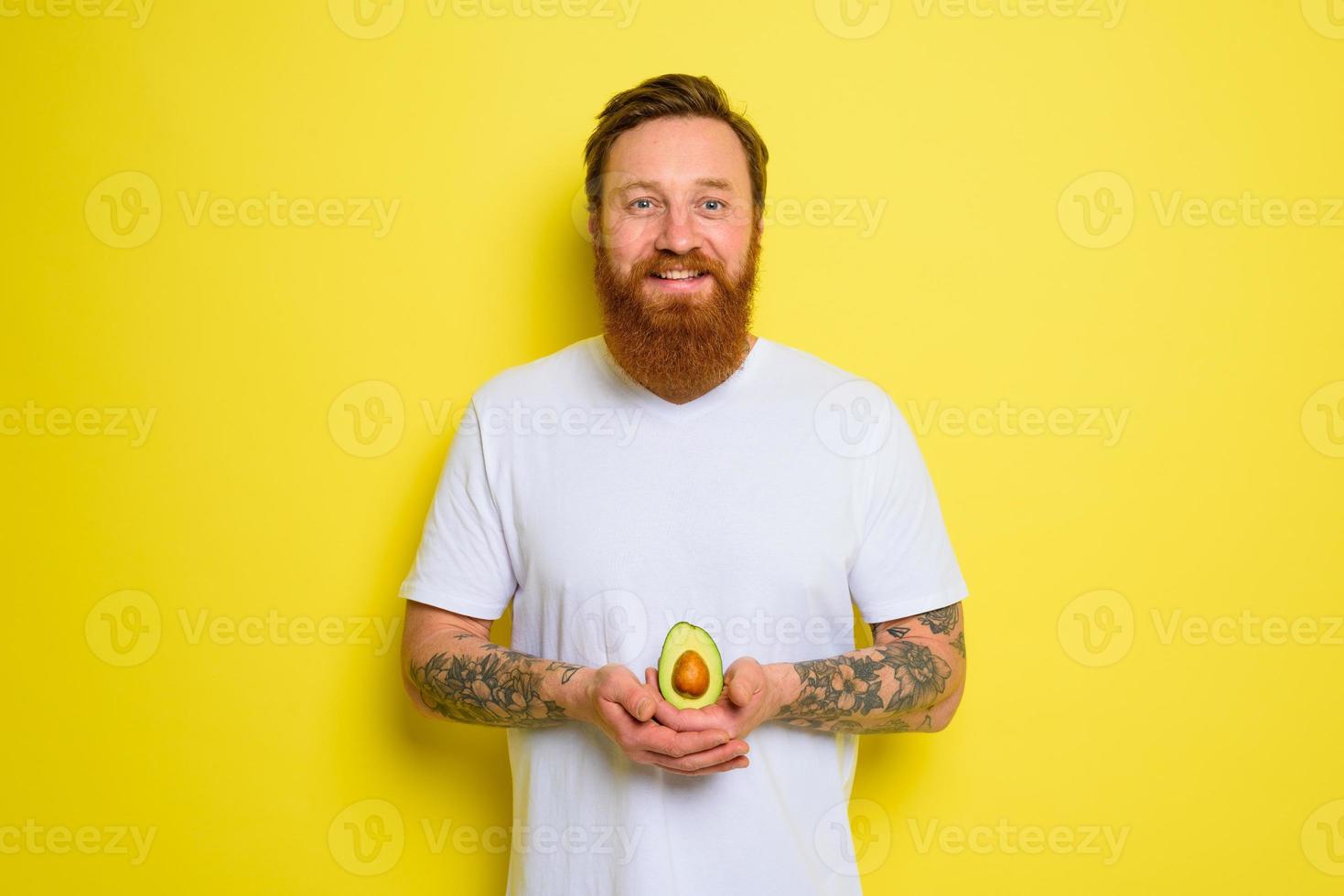 Happy man with beard and tattoos holds an avocado photo