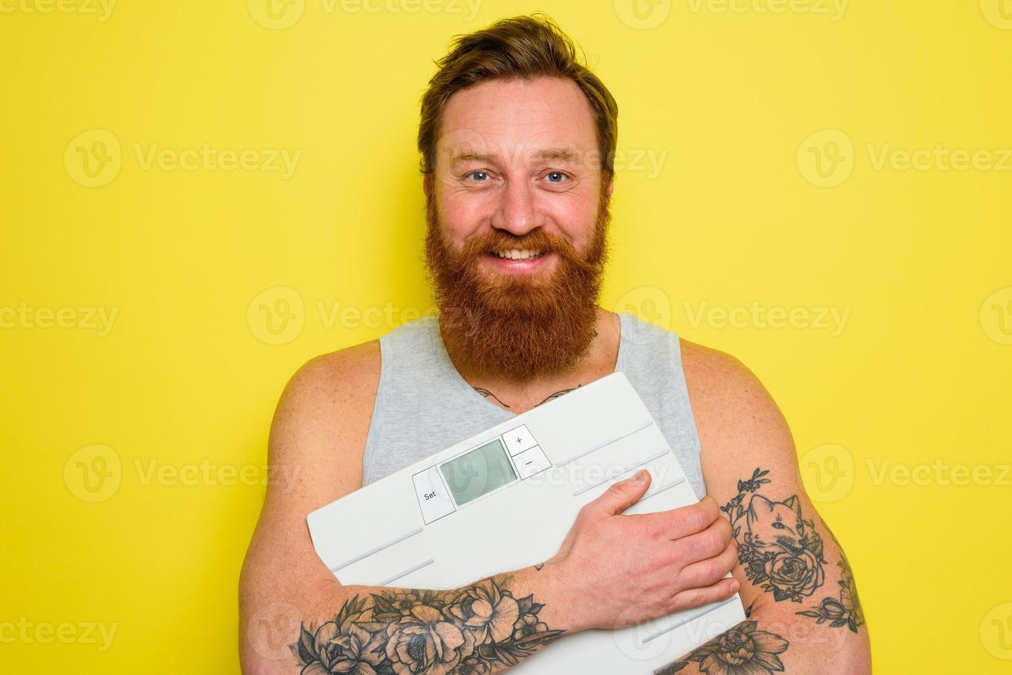 Happy man with beard and tattoos holds an electronic balance photo