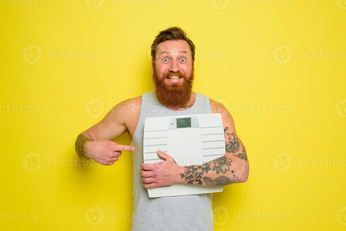 Amazed man with beard and tattoos holds an electronic balance photo