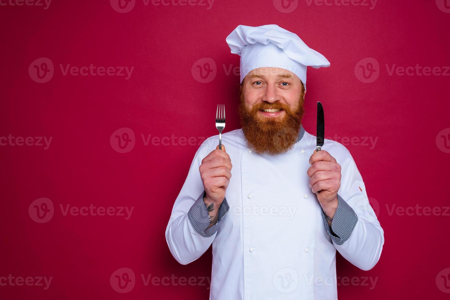 happy chef with beard and red apron holds cutlery in hand photo