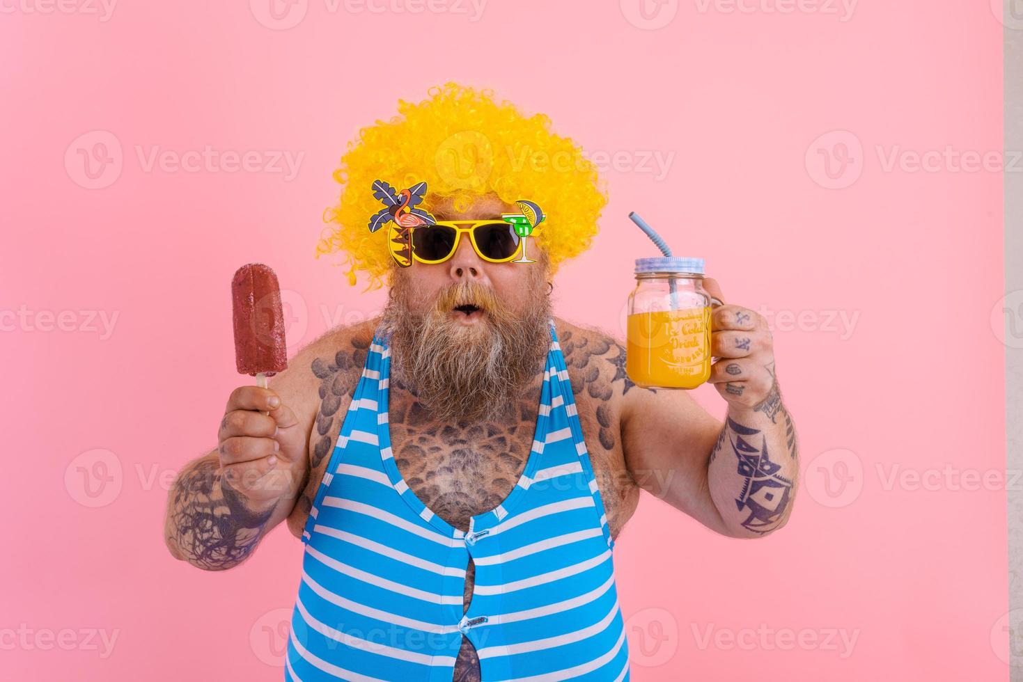 Fat surprised man with beard and wig eats a popsicle and drinks a juice fruit photo