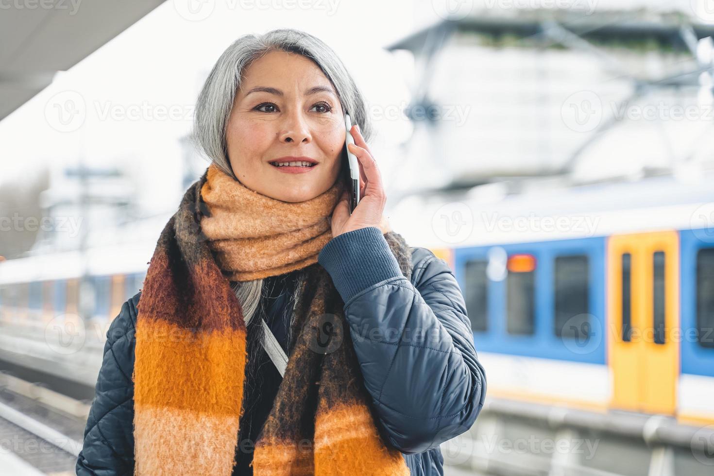 Senior woman send message with a mobile phone and waits for a train photo