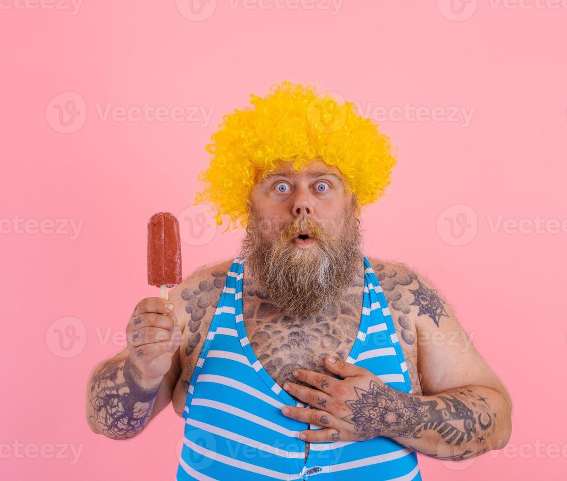 Fat amazed man with beard and wig eats a popsicle photo